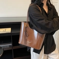Dark brown high-gloss tote bag with H-pendant charm on a black outfit background - With Charm / Brown