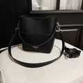 Detail of black lychee grain leather bucket bag with silver hardware on white stool - Black