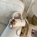 Detail of cream cylinder handbag with plush bear charm on a soft fabric sofa - With Charm / White