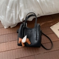Detail view of black pebble leather bucket bag with brown horse charm on a wooden surface - With Pendant / Black