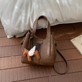 Brown lychee leather bucket bag with pegasus charm on a rustic wooden floor - With Pendant / Coffee