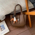 Detail of brown litchi pattern bucket bag featuring a silver lock and pegasus charm - With Charm / Coffee