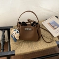 Sac seau en cuir marron avec fermoir argenté et petit charm chien posé sur un tabouret - Avec Pendentif / Marron