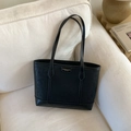 Detail of minimalist black leather tote bag with metal logo on a cozy home sofa - Black