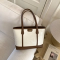 Detail shot of a vintage beige tote bag with brown handles on a cozy sofa setting - White