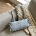 Bolso baguette azul grisáceo claro con lazos laterales sobre un sofá acogedor - Azul