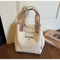 Detail der Canvas-Beuteltasche mit geblümten Griffen und Text auf dunklem Holzboden - Gebrochenes Weiß