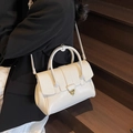 Minimalist white leather handbag with gold rotating clasp shown in a lifestyle setting - Off-white