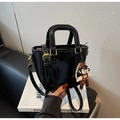 Detail der schwarzen Handtasche mit Gold-Hardware und niedlichem Puppen-Perlenanhänger - Schwarz mit Anhänger