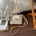 Gros plan d'un sac carré crème avec un pendentif ours en peluche dans un intérieur - Blanc avec pendentif