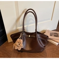 Detailansicht der dunkelbraunen Leder-Shopper auf Holzboden mit Plüschbären-Anhänger - Mit Anhänger / Braun