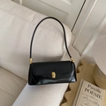 Detail of black rectangular baguette bag with gold metal clasp on a sofa - Black