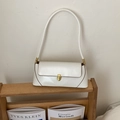 Detail of white vintage baguette bag with brown piping and gold clasp on a wooden stand - White
