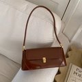 Chic brown baguette underarm bag with glossy finish and vintage gold buckle on a sofa - Brown
