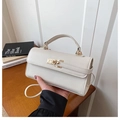 Detail of cream leather handbag with lychee texture and gold twist lock in indoor setting - White