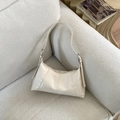 Detail of creamy white leather crescent bag with stitched seams on a beige sofa - White