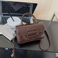 Detail of a dark brown glossy handbag featuring a prominent large metal square buckle - With Pendant / Brown