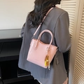 Pink faux leather bucket bag with wood bead tassel shown on a shoulder - Pink