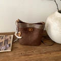 Detail of suede bucket bag with gold clasp and decorative horse charm on wood surface - Brown