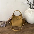 Detail of mustard yellow bucket bag with golden hardware and bear charm on wooden desk - Caramel (With Charm)
