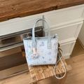 Detail view of a floral cartoon tote bag with rabbit charm on a woven stool - Blue