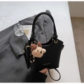 Detail of black lychee texture bucket bag with bear charm on grey suit background - Black With Pendant