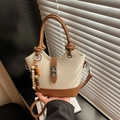 Detailed shot of beige leather bucket bag featuring metal buckle and beaded charm - White and Brown