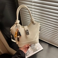 Close-up of cream white bucket bag featuring silver twist lock and wooden beaded charm - White