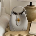 Sac seau gris clair texture litchi avec fermoir en T doré posé sur table en bois - Gris