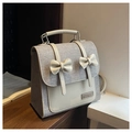 Detalle de mochila estilo preppy con tejido gris, cuero crema y dos lazos decorativos - Gris