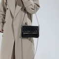 Chic black suede crossbody bag with silver studs and chain strap shown on a model - Black