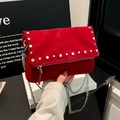 Red suede crossbody bag with silver stud trim and chain strap held by a model - Red