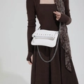 White crossbody bag with silver studs and metal chain strap shown on a model - White