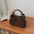 Detail of dark brown woven bucket bag with unique knot handle design on wooden desk - Brown