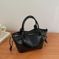 Detail of black leather handbag with braided handle knots and gold hardware on wood surface - Black