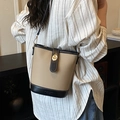 Bolso saco beige con ribete de cuero negro y cierre dorado llevado por una modelo - Caqui