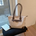 Detalle del bolso tote de lona con acabados en cuero marrón sobre un taburete - Gris Beige