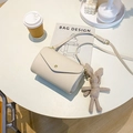 Off-white schoudertas met kiezeltextuur en konijntjeshanger op een moderne tafel - Beige met Hanger