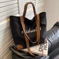Sac cabas en toile noire avec poignées en cuir marron et bandoulière sur un canapé - Noir