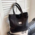 Minimalist black canvas tote bag for women with SHANGCAI label on a leather sofa - Black