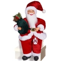Zittende kerstmanpop in rood fluweel met groene cadeauzak en witte lantaarn - Rode Kerstman