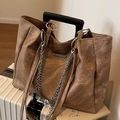 Bolso tote grande marrón oscuro con cadena plateada sobre una maleta blanca - Caqui