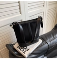 Dettaglio di una borsa a secchiello nera opaca con finiture dorate su un libro bianco - Nero