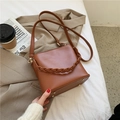 Borsa a secchiello caramello con manico intrecciato e rivetti dorati su sfondo chic - Marrone