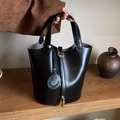 Schwarze Leder-Eimertasche mit Goldschloss und Smiley-Anhänger auf Holzständer - Schwarz