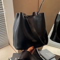 Schwarze Bucket Bag aus Leder mit breitem Schultergurt und goldener Aufschrift in der Hand - Schwarz