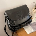 Black PU leather crossbody bag with shield patch and silver chain on a wooden table - Black