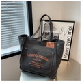 Detail of dark grey canvas tote bag featuring orange letter print and leather label patch - Dark Brown