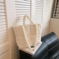White quilted puffer tote bag with square stitching placed on black leather sofa - White