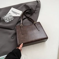 Dark brown retro textured tote bag with gold buckle straps on a grey blazer backdrop - Brown